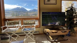 A room with a large window offering a mountain view, a television, a Christmas tree, and a folding chair with a map. - Cozy Cabin (Silverthorne)