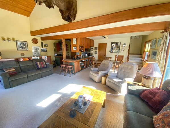 A spacious living room with a sofa, armchairs, and a coffee table. A kitchen area is visible in the background.
