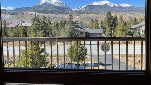 A view from a window overlooking a snowy mountain range, with a clear sky and a few buildings in the foreground. - Cozy Cabin (Silverthorne)