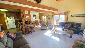 A spacious living room with a large sofa, a coffee table, and a dining area with wooden chairs and a kitchen in the background. - Cozy Cabin (Silverthorne)