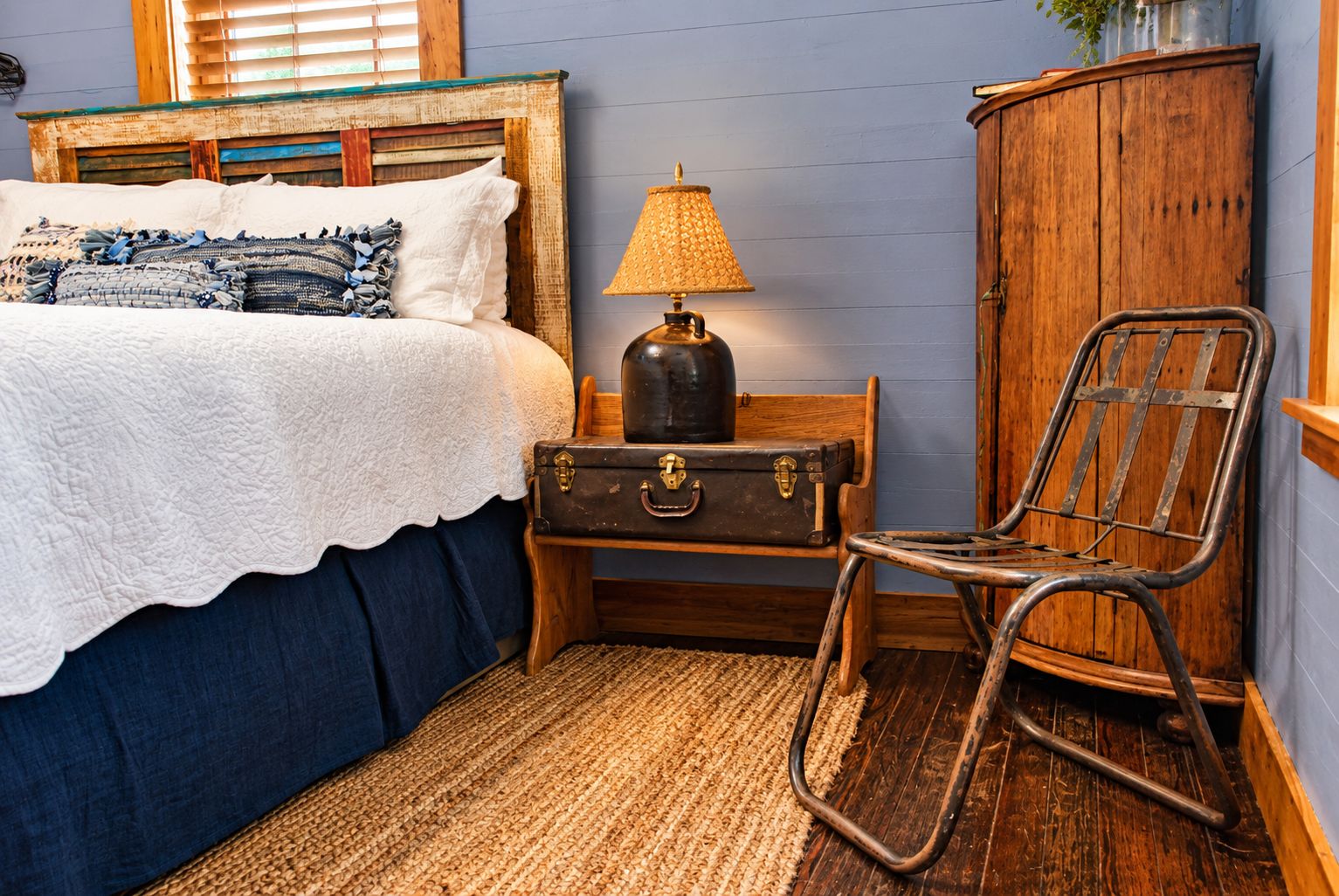 A bedroom with a bed, a lamp, a suitcase, a chair, and a wooden cabinet.