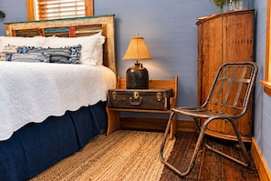 A bedroom with a bed, a lamp, a suitcase, a chair, and a wooden cabinet.