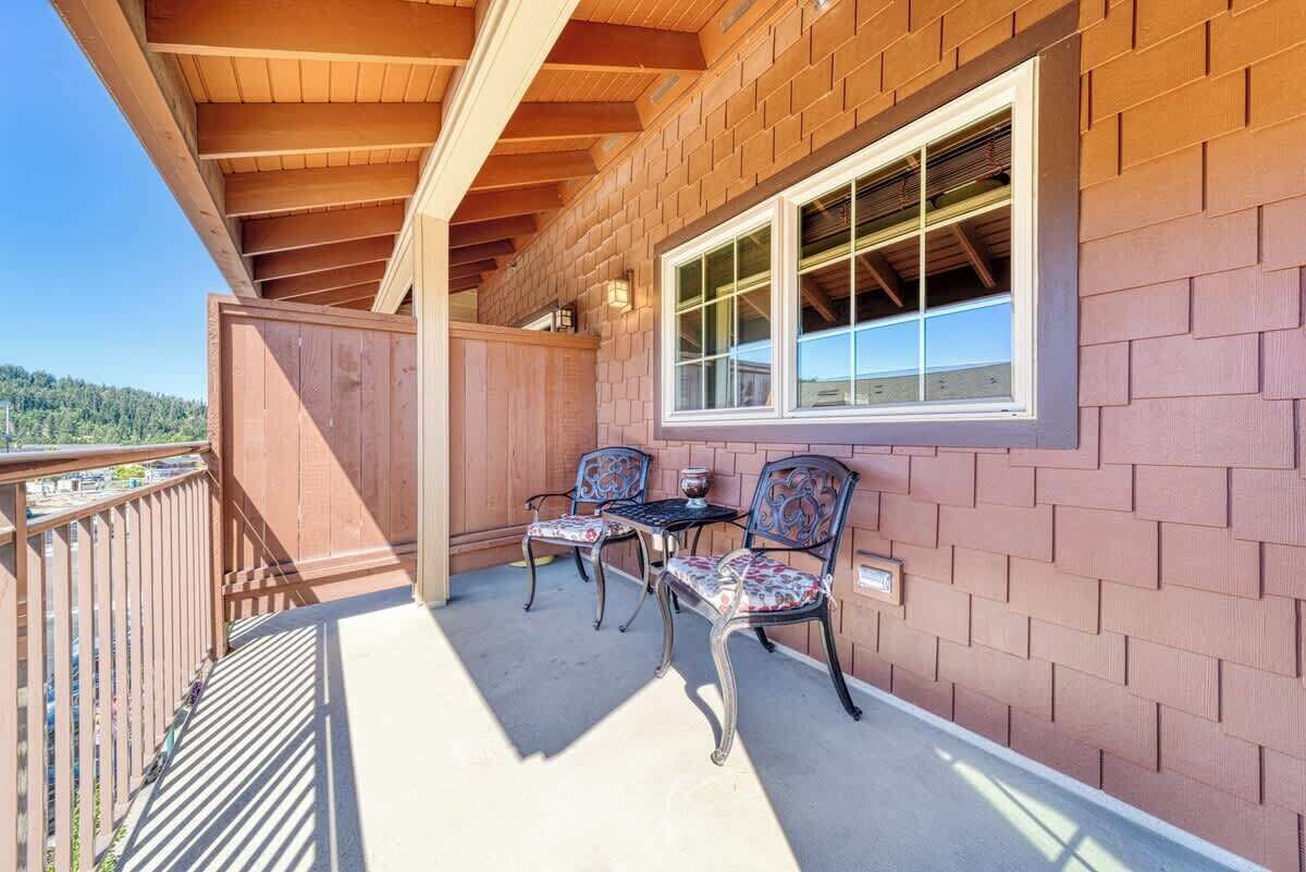 A balcony with two chairs and a table, wooden beams, and a brick wall.