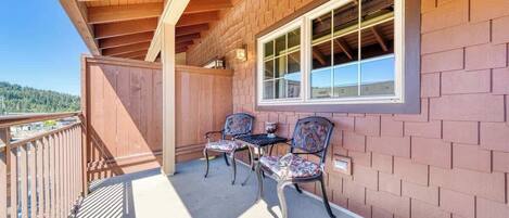 A balcony with two chairs and a table, wooden beams, and a brick wall.