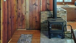 Interior rústico de una cabaña con chimenea de piedra, paredes de madera y un manguera contra incendios visible.