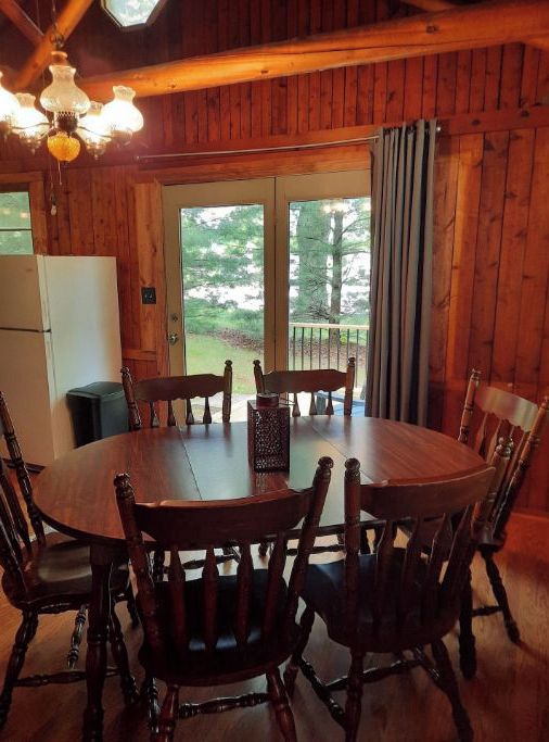 Ein Esszimmer mit Holzboden, einem runden Tisch und sechs Stühlen, einem Kühlschrank und einem Fenster mit Vorhängen.