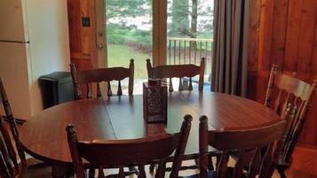 Une salle à manger en bois avec une table ronde et six chaises, un réfrigérateur et une fenêtre avec des rideaux.