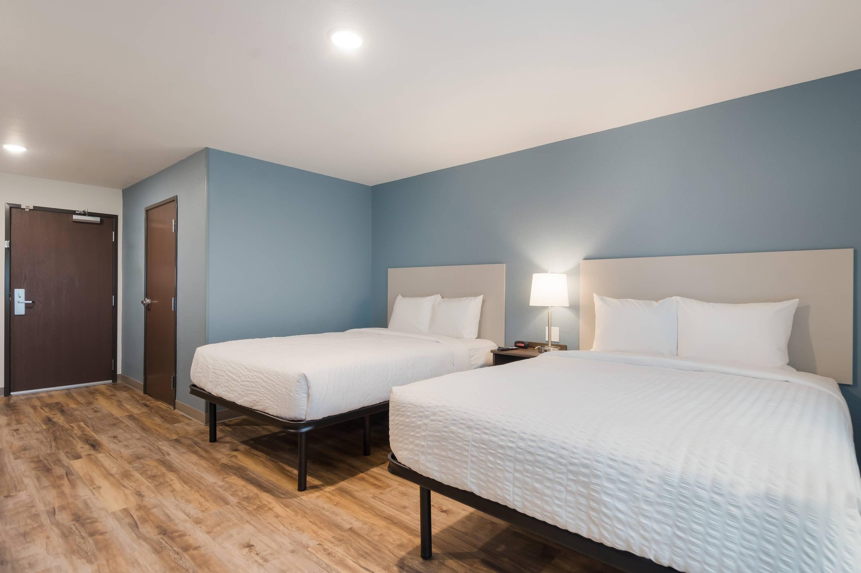 A hotel room with two beds, a wooden floor, and a blue wall.