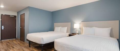 A hotel room with two beds, a wooden floor, and a blue wall.