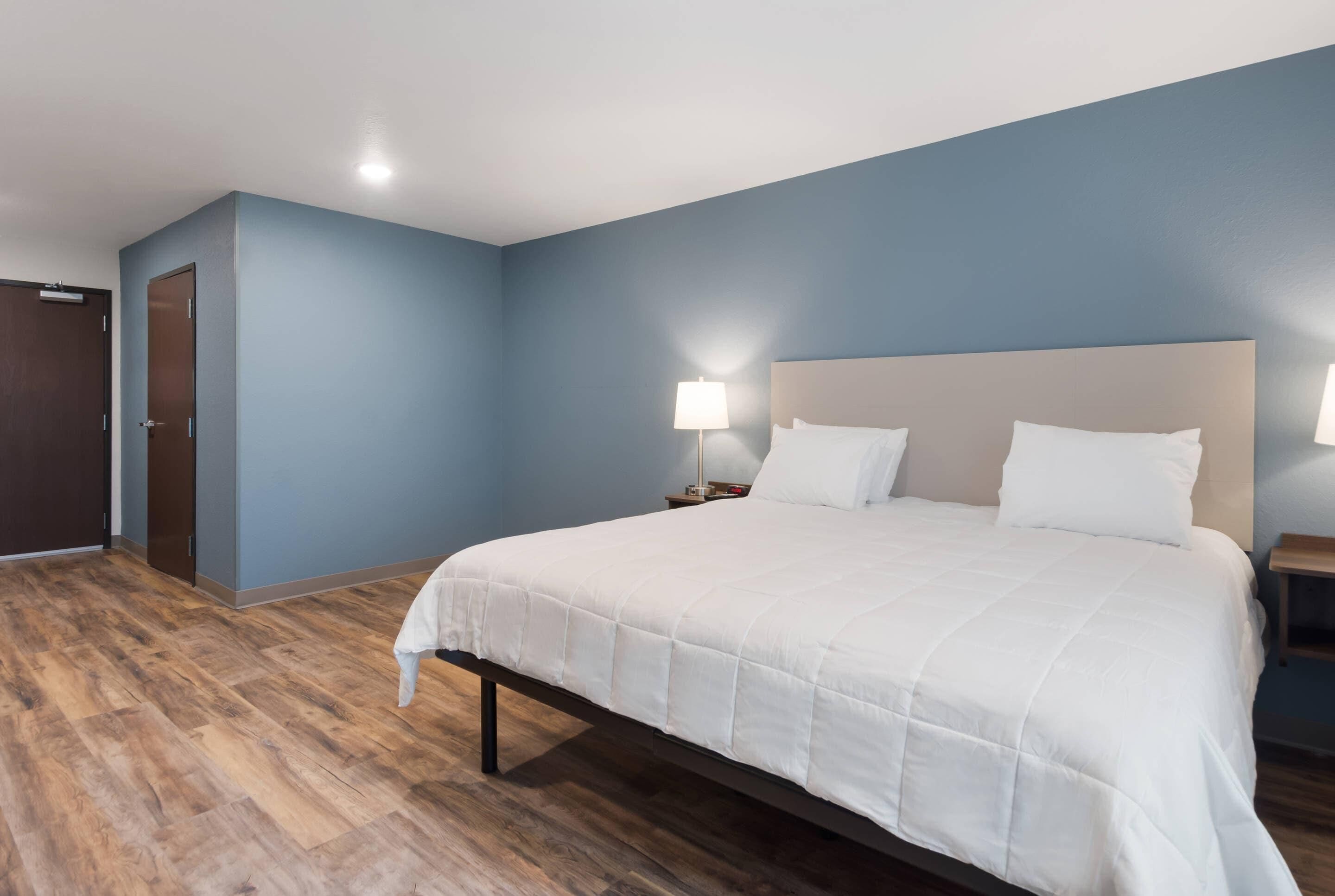 Una habitació d'hotel amb un llit gran, una nit del costat amb una làmpada i un terra de fusta.