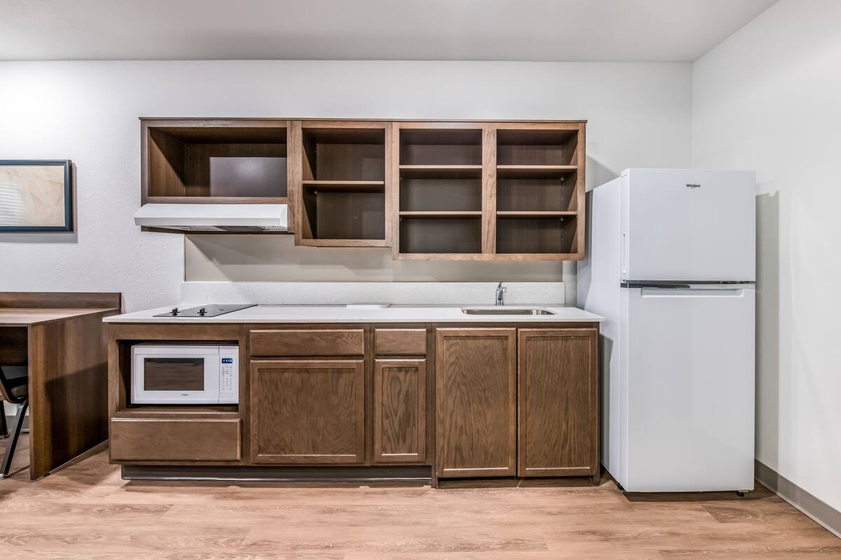 A kitchen with wooden cabinets, a microwave, a sink, and a white refrigerator.