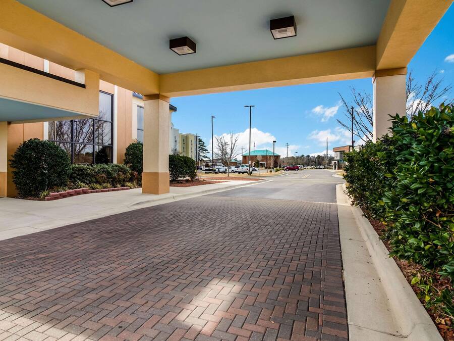 A spacious outdoor area with a paved walkway, a covered seating area, and a clear view of the parking lot and buildings in the background.