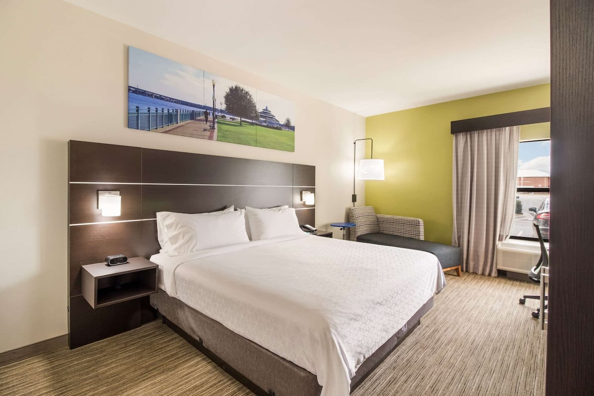 Quarto de hotel com uma cama grande, uma mesa de cabeceira com abajur, uma pequena escrivaninha e uma cadeira.