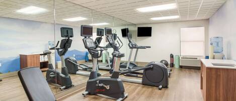 A gym with cardio machines, a mirrored wall, and a water dispenser.