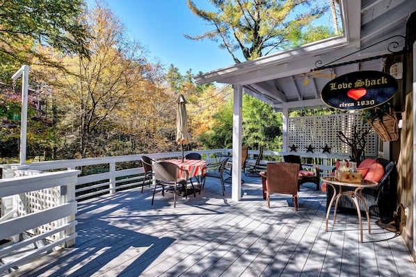 A covered outdoor deck with a sign reading "Love Shack circa 1930". - Waterfall Bungalow: Quaint Cottage on Mill Creek w/ Deck | Walk to Downtown (Highlands)