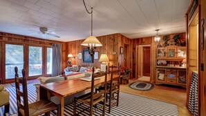 A wooden interior with a dining table, chairs, and a chandelier. There are windows and a door leading to another room. - Waterfall Bungalow: Quaint Cottage on Mill Creek w/ Deck | Walk to Downtown (Highlands)