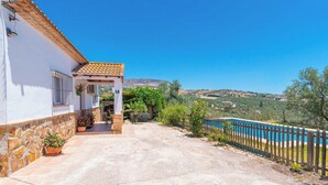 Une maison avec un mur en pierre, un toit en tuiles et une vue sur une piscine bleue et des collines.