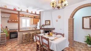 Une cuisine chaleureuse avec un coin repas, agrémentée d’une cheminée en briques, de meubles en bois et d’un lustre.