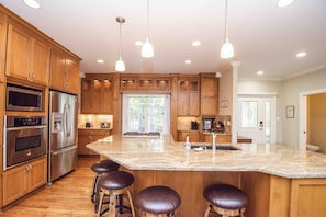 Una cocina moderna con armarios de madera, electrodomésticos de acero inoxidable, una isla grande con taburetes de bar e iluminación colgante.