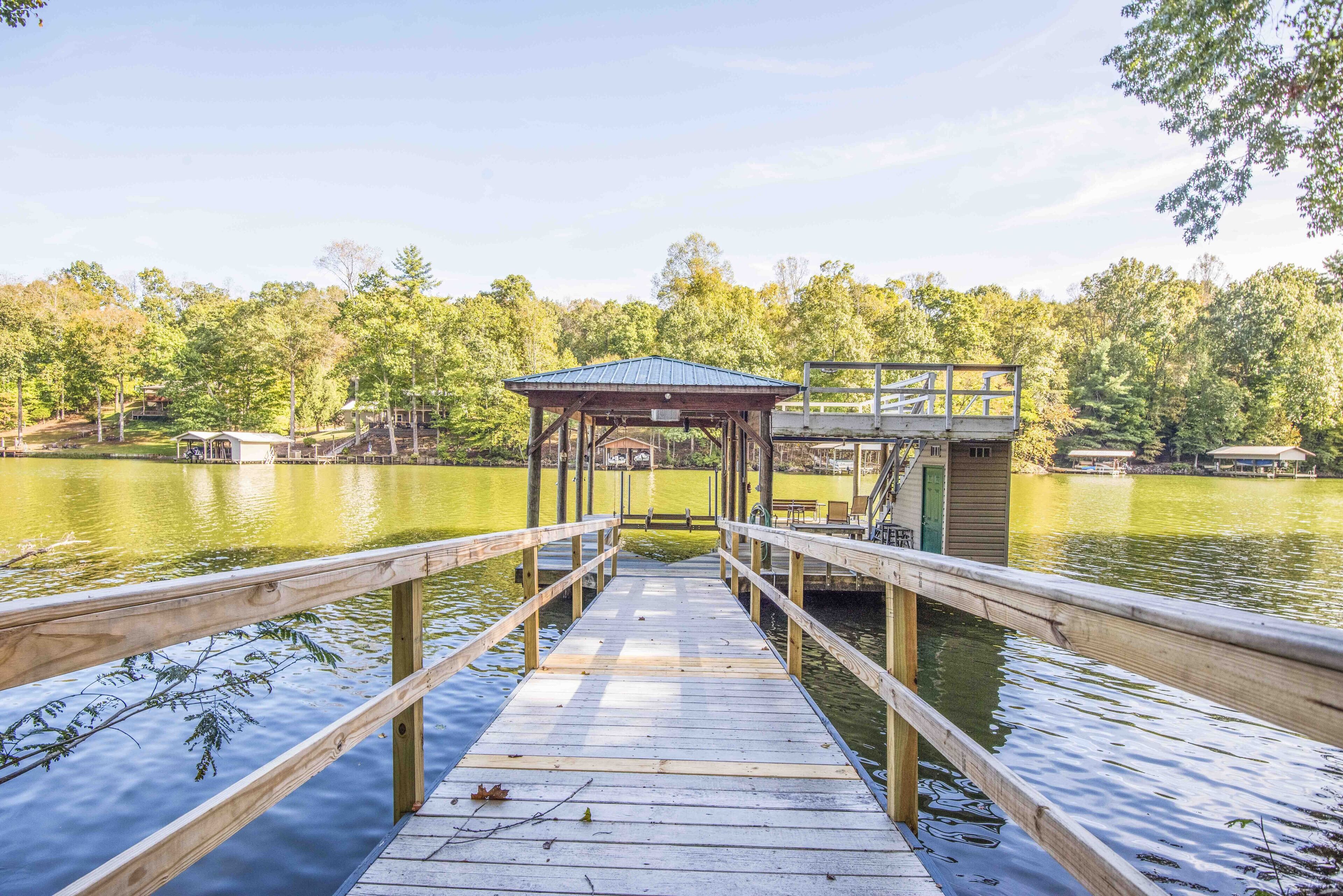 A wooden dock leading to a covered area with a view of a lake and trees.
