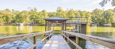A wooden dock leading to a covered area with a view of a lake and trees.