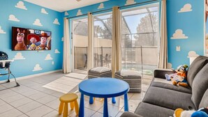 A living room with a blue wall, a ceiling fan, a TV, a gray sofa, a blue table, and a window with curtains. - Windsor Hills Resort/3Bed/POOL/Near Disney (Kissimmee)