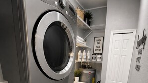 A laundry room with stacked washers and dryers, a shelf with laundry supplies, and a door with a laundry-related sign.