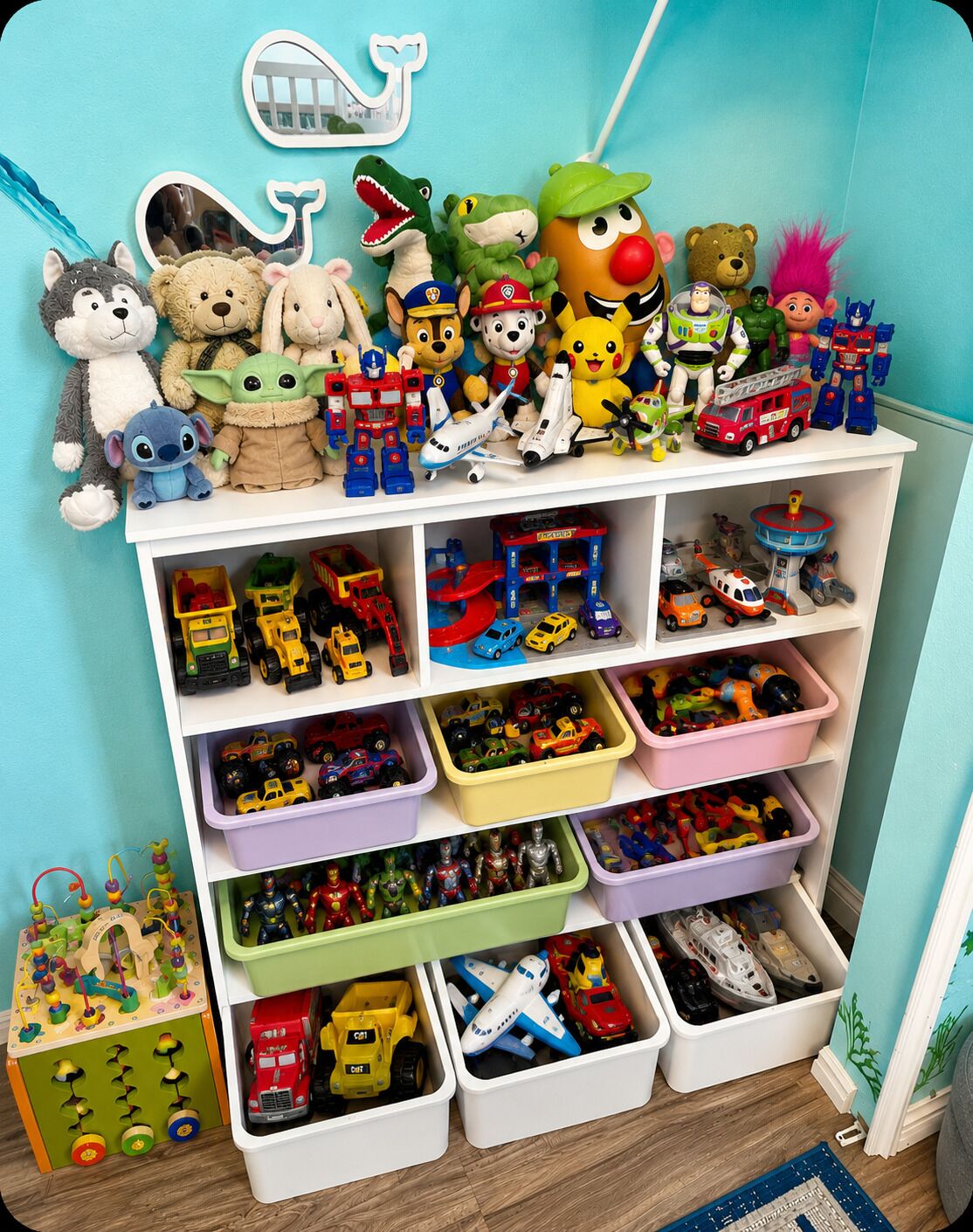 A room with a wall-mounted shelf holding various plush toys and figurines. Below, there are multiple storage bins with toys and vehicles.