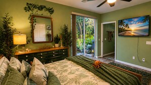 A bedroom with a bed, a dresser, a mirror, a ceiling fan, a TV, and a view of the outdoors.