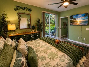 Un dormitorio con cama, cómoda, espejo, ventilador de techo, televisor y vistas al exterior.