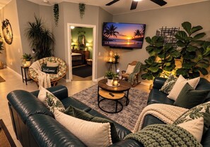 Een moderne woonkamer met een leren bank, een ronde salontafel en een televisie waarop een zonsondergang te zien is.