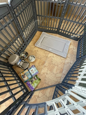 Ein tierfreundliches Zimmer mit einem Metallgitter, einem Tierbett, Näpfen und Tierfutterverpackungen.