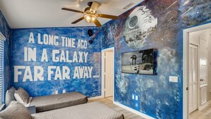 Un dormitorio con un mural temático de galaxia, un ventilador de techo y una cama con almohadas.