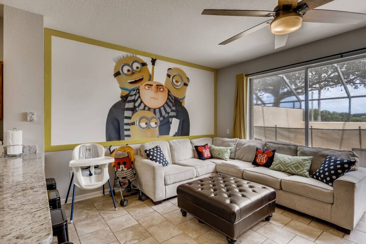 A living room with a large wall mural, a sofa set, a high ceiling fan, and a view through a large window.