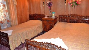 Quarto com duas camas, cabeceiras de madeira, uma mesinha de cabeceira com um vaso e um arranjo floral na parede.