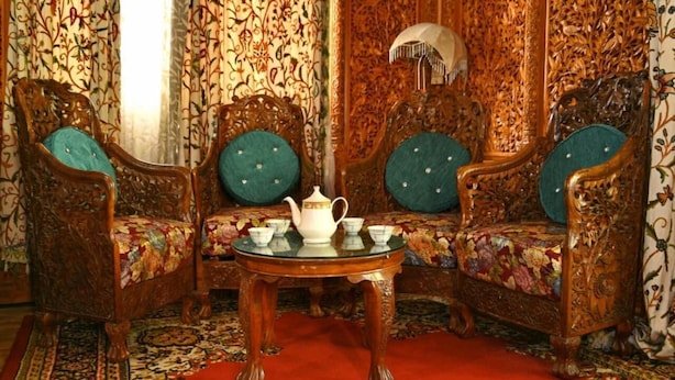 Um quarto com móveis de madeira ornamentados, uma mesa central com jogo de chá e cortinas estampadas.
