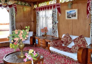 A wooden interior with a sofa, a table with a vase of flowers, and curtains. - De Laila House Boat (Srinagar)