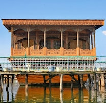 A traditional wooden structure with intricate carvings, supported by pillars, and situated over water.