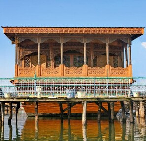 A traditional wooden structure with intricate carvings, supported by pillars, and situated over water. - De Laila House Boat (Srinagar)