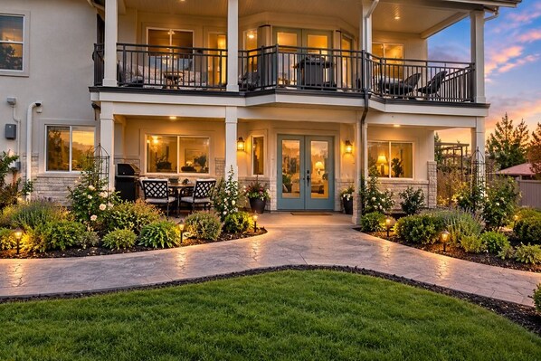 A two-story house with a balcony, a front door, and a patio area with outdoor furniture.