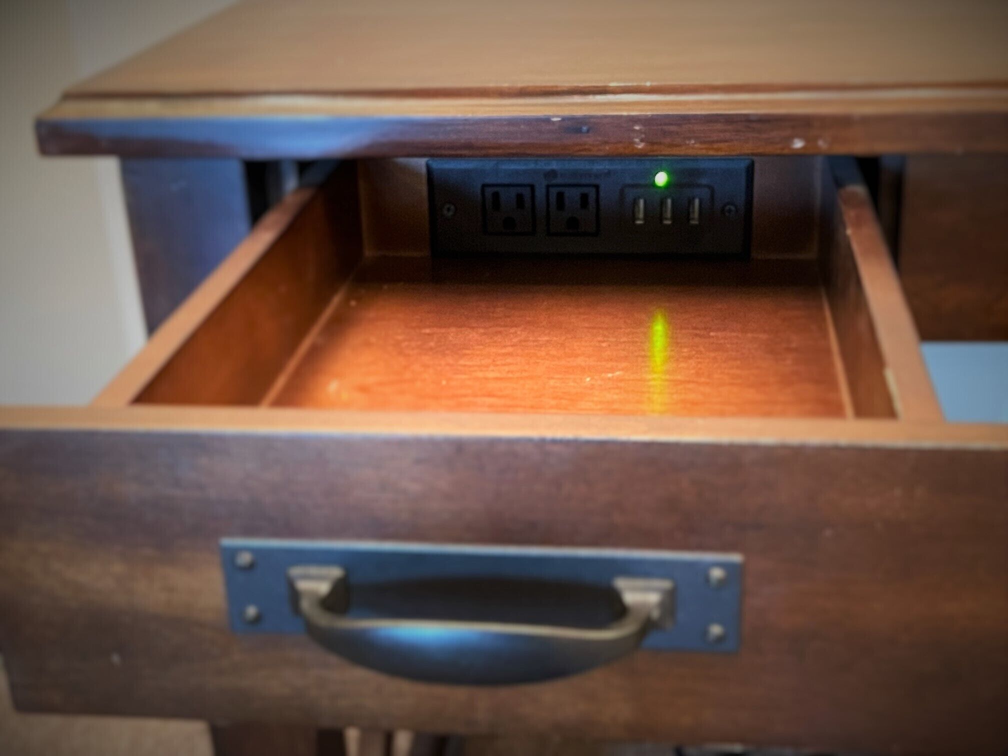 A wooden drawer with a metal handle and a power strip with a green light.