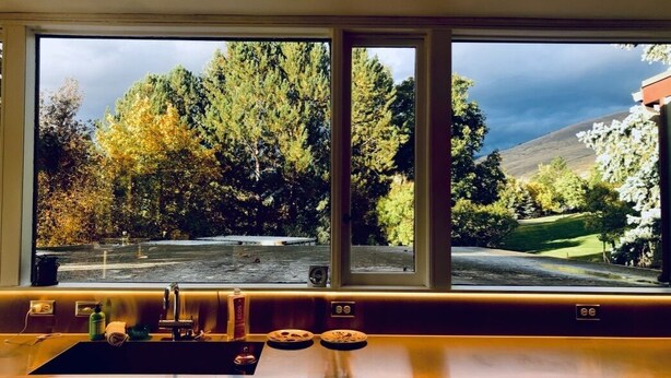 A kitchen with a large window overlooking a park and trees.