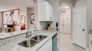A modern kitchen with granite countertops, stainless steel sink, white cabinets, and a built-in dishwasher. - Windsor Hills Resort/3Bedrm Themed Condo (Kissimmee)