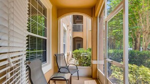 A balcony with two chairs and a table, overlooking a garden with trees and shrubs. - Windsor Hills Resort/3Bedrm Themed Condo (Kissimmee)