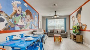 A dining area with a blue table and chairs, a sofa, a TV stand, and a ceiling fan. - Windsor Hills Resort/3Bedrm Themed Condo (Kissimmee)
