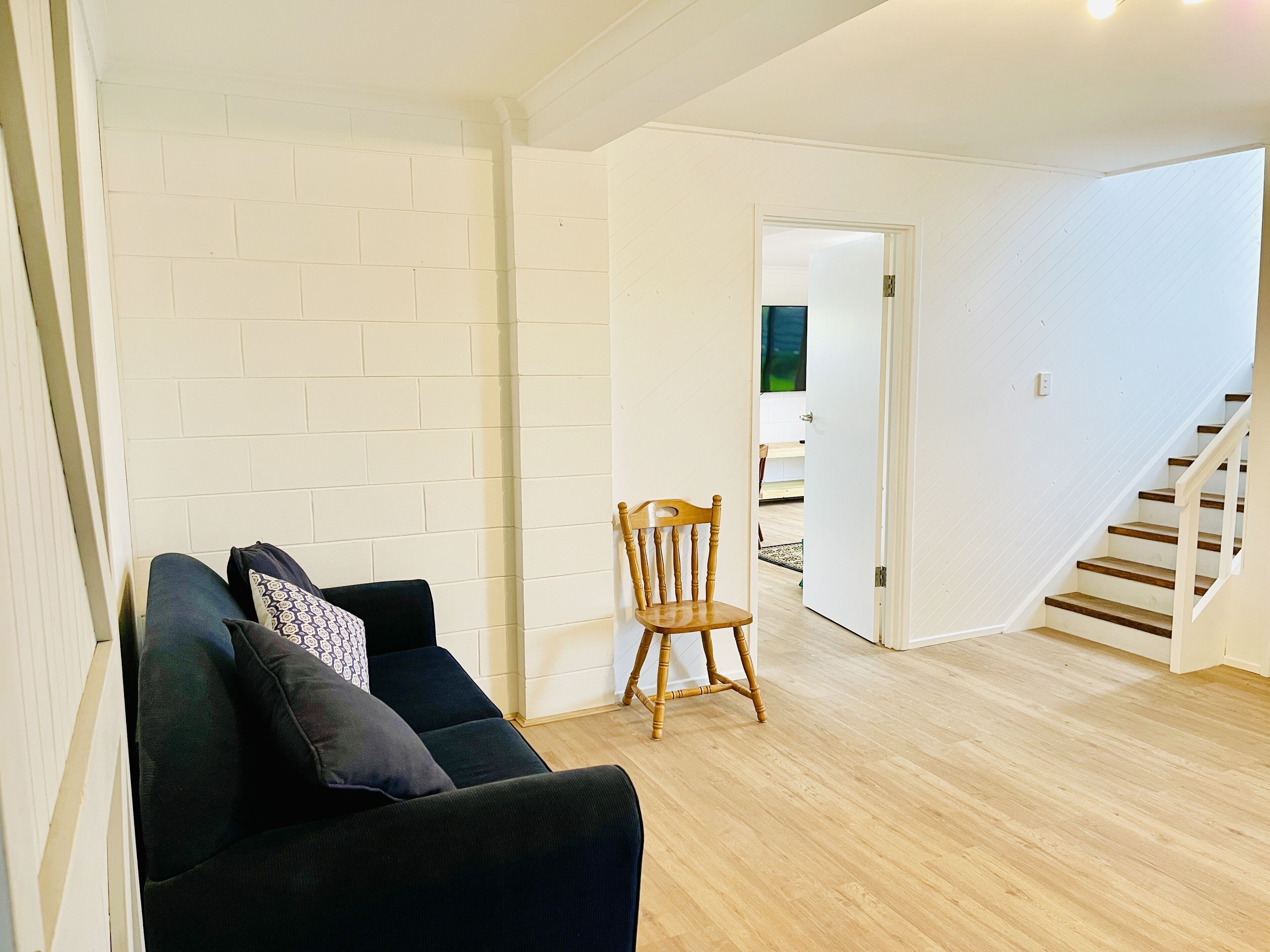 Una sala de estar con un sofá negro, una silla de madera y una pared de ladrillo blanco.