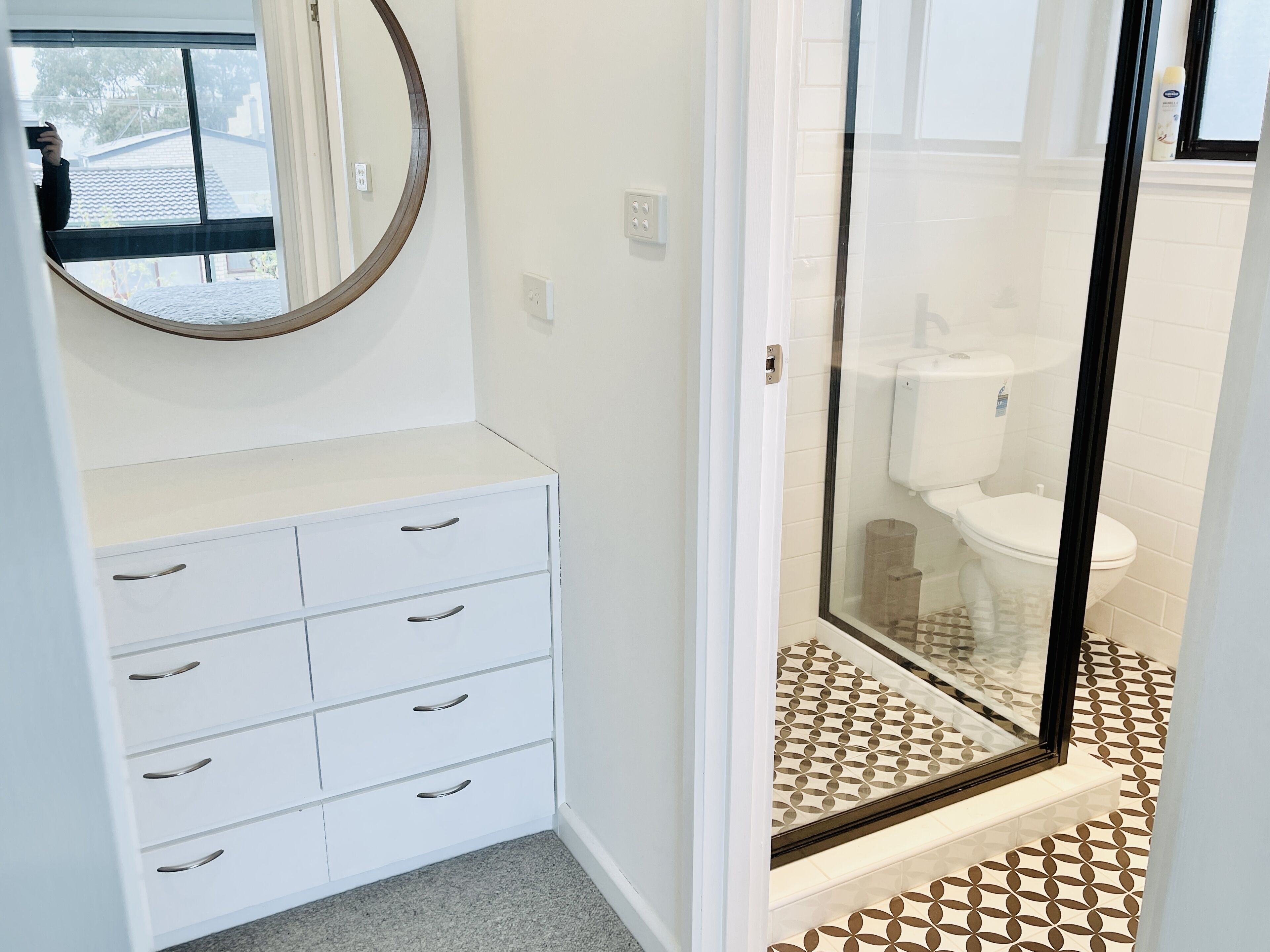 A bathroom with a white vanity, a round mirror, and a glass shower enclosure.