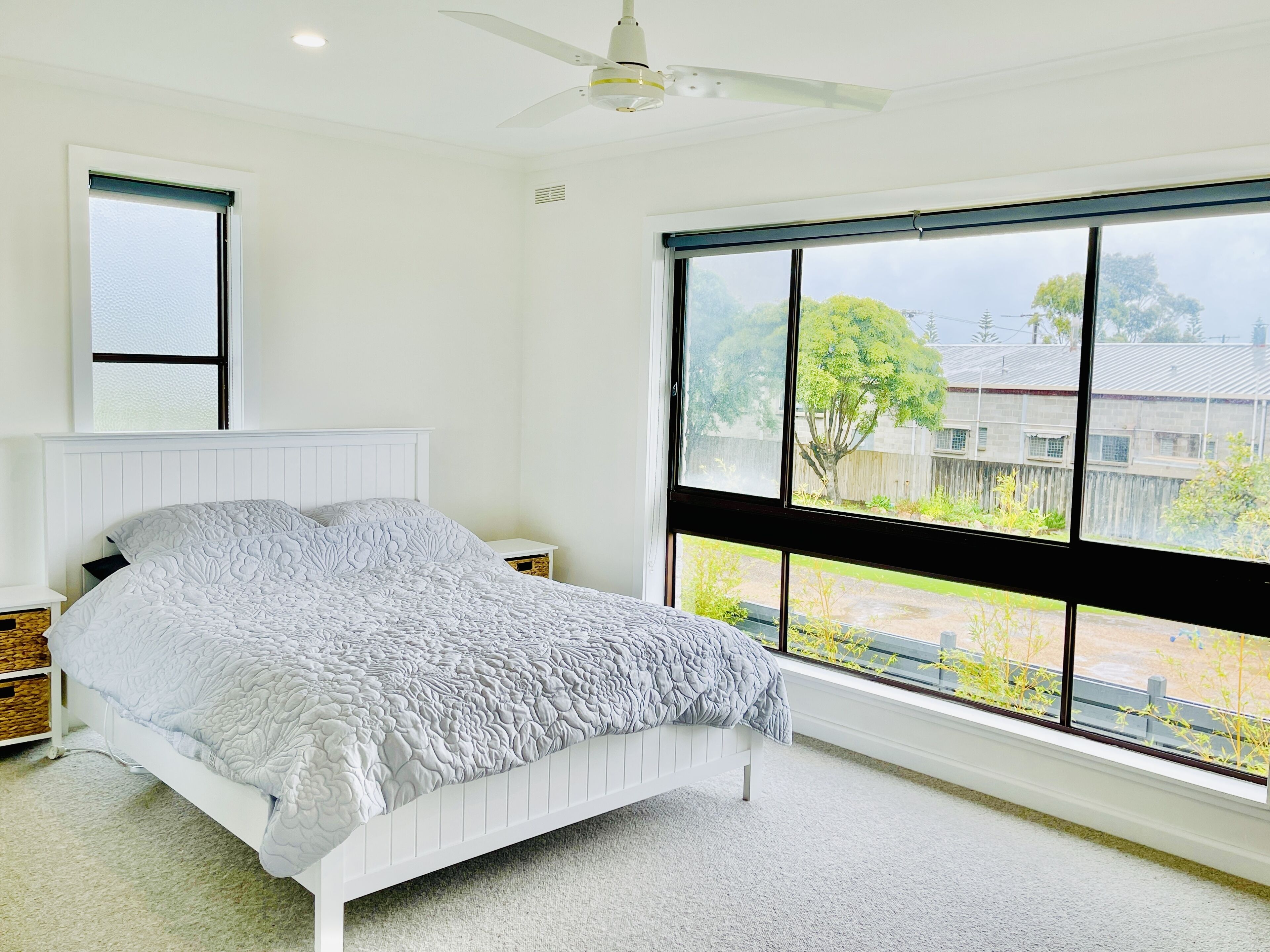 A bedroom with a large window, a bed, and a ceiling fan.