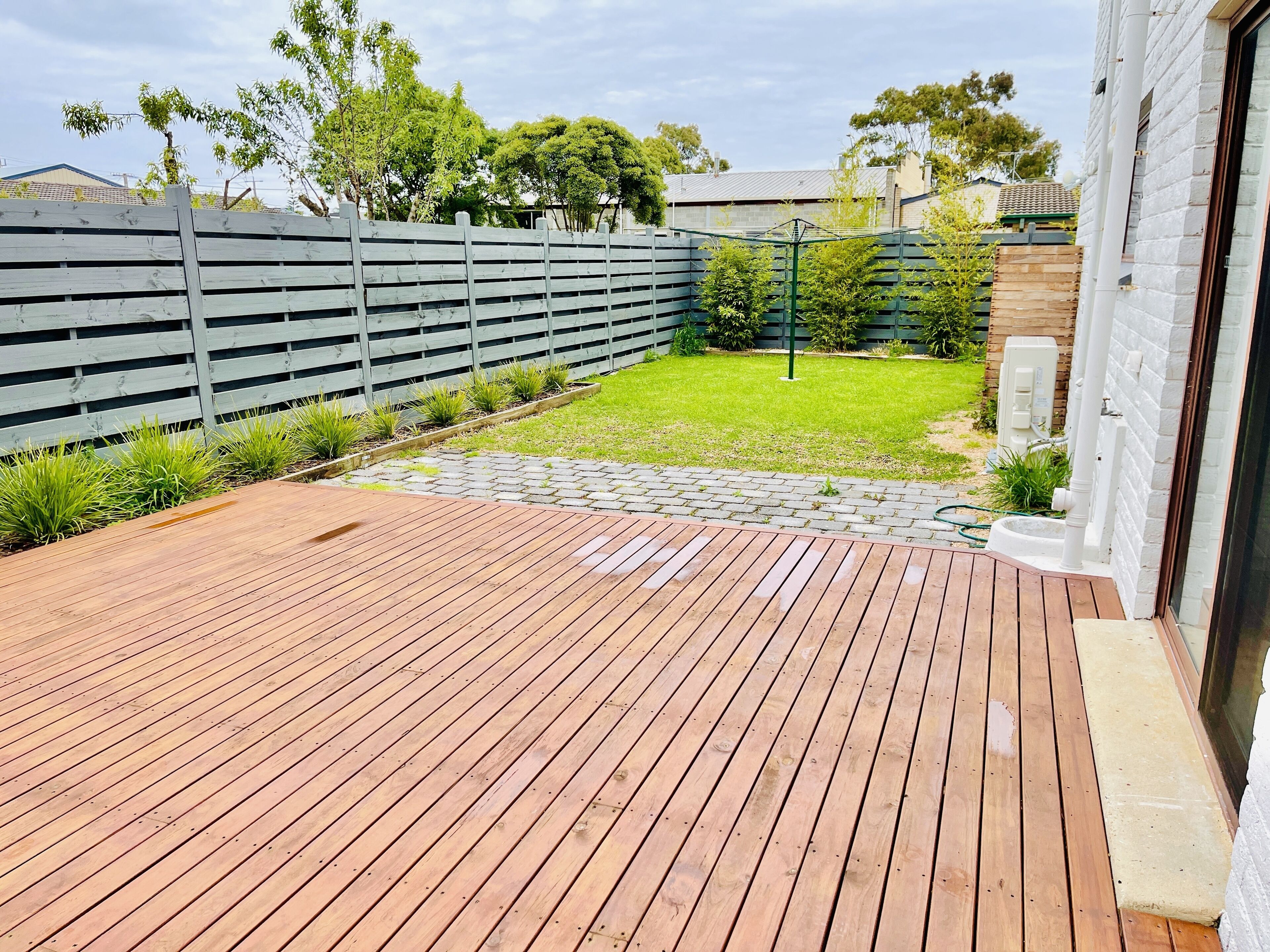 A wooden deck with a stone pathway leading to a grassy area, surrounded by a wooden fence and trees.