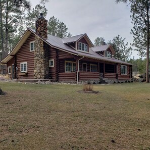 A log cabin with a stone chimney, large windows, and a porch. - Two story authentic log construction home, built in 1936 with two fireplaces. (Custer)